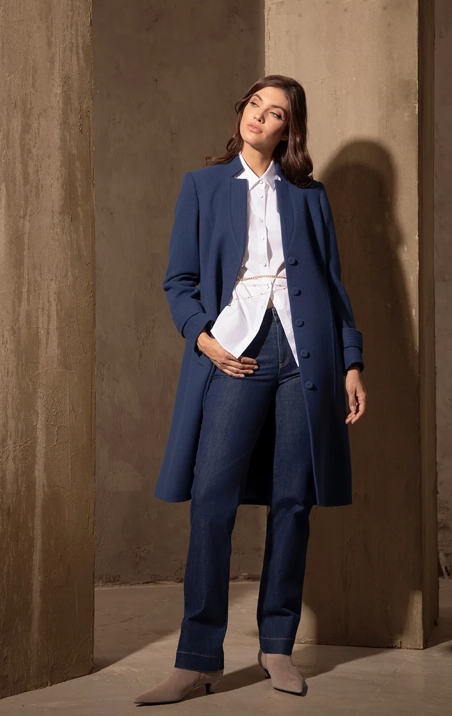 Elegant women’s look with blue coat, white shirt and dark blue jeans