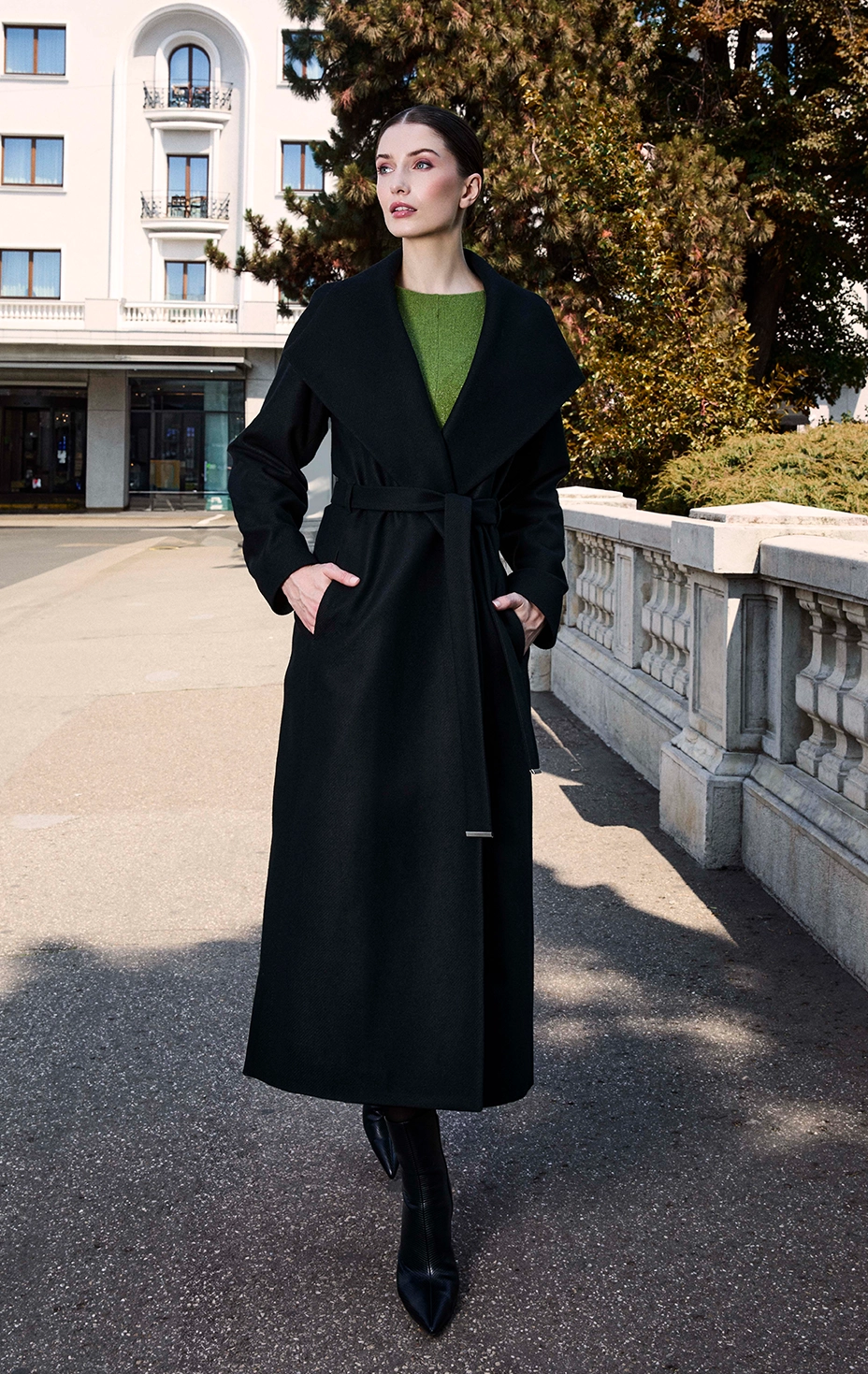 Woman in an elegant black belted coat over a green flared dress. Dika sophisticated look.